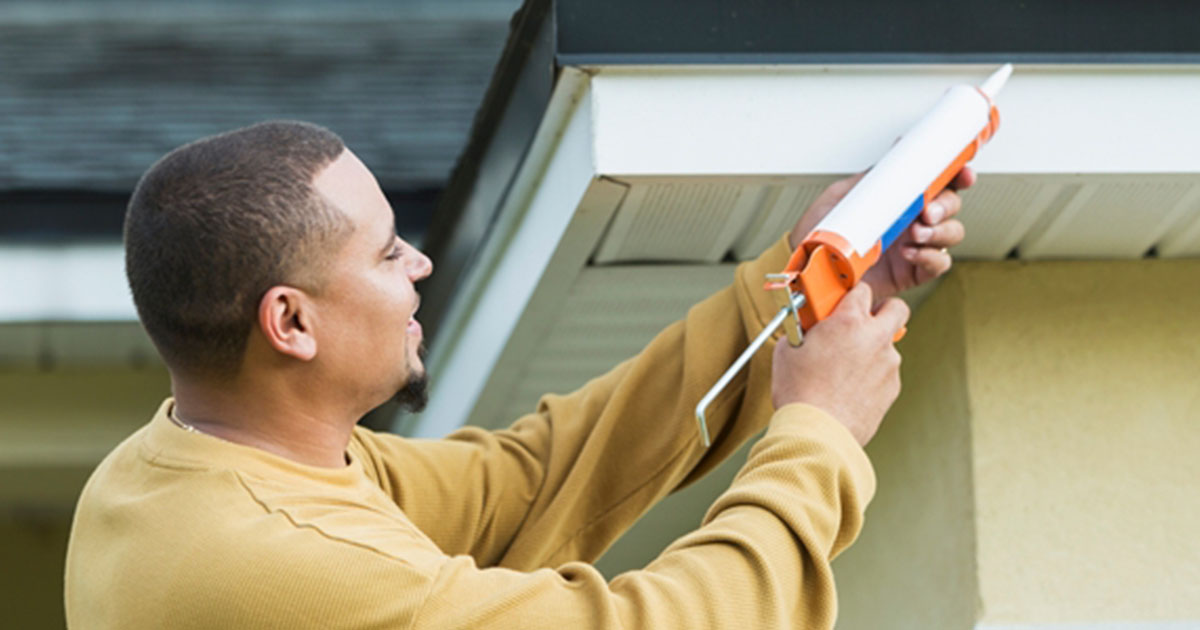 Man applying caulk to exterior of house gutter
